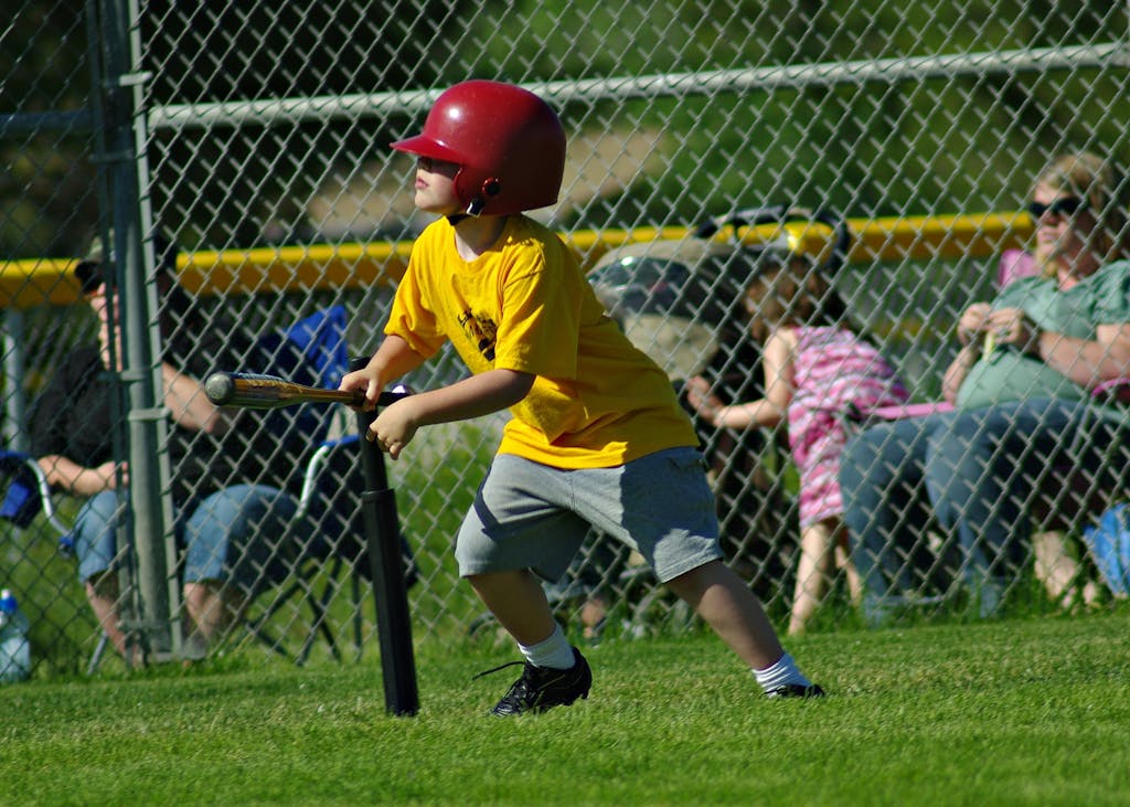 Child in a yellow shirt and helmet playing baseball outdoors on a sunny day.