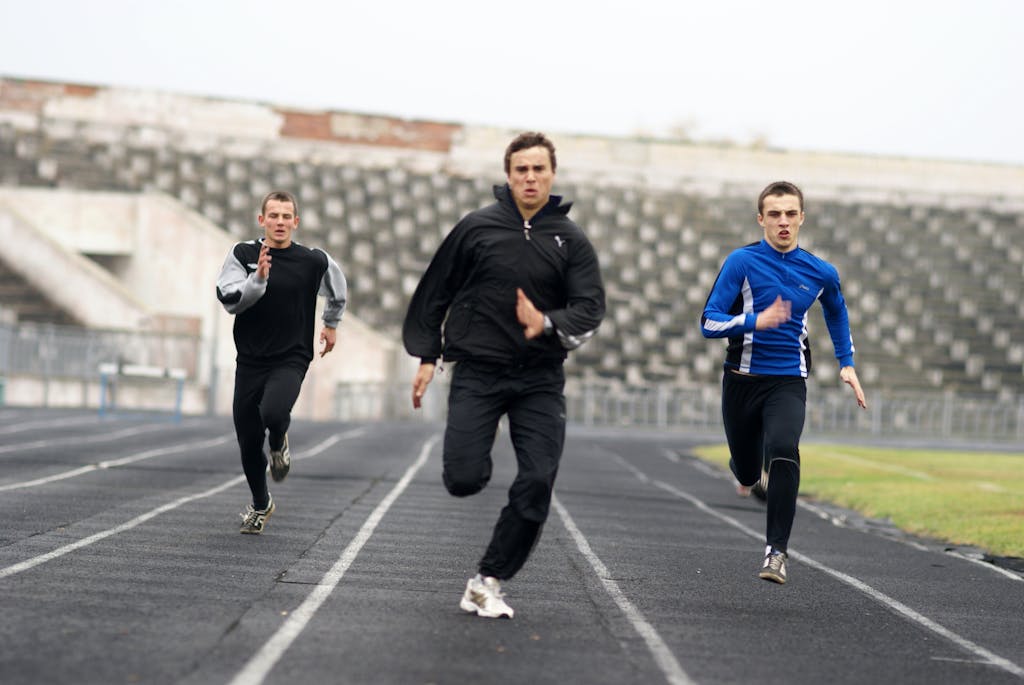 Three athletes intensely sprint down a stadium track, showcasing determination and speed.