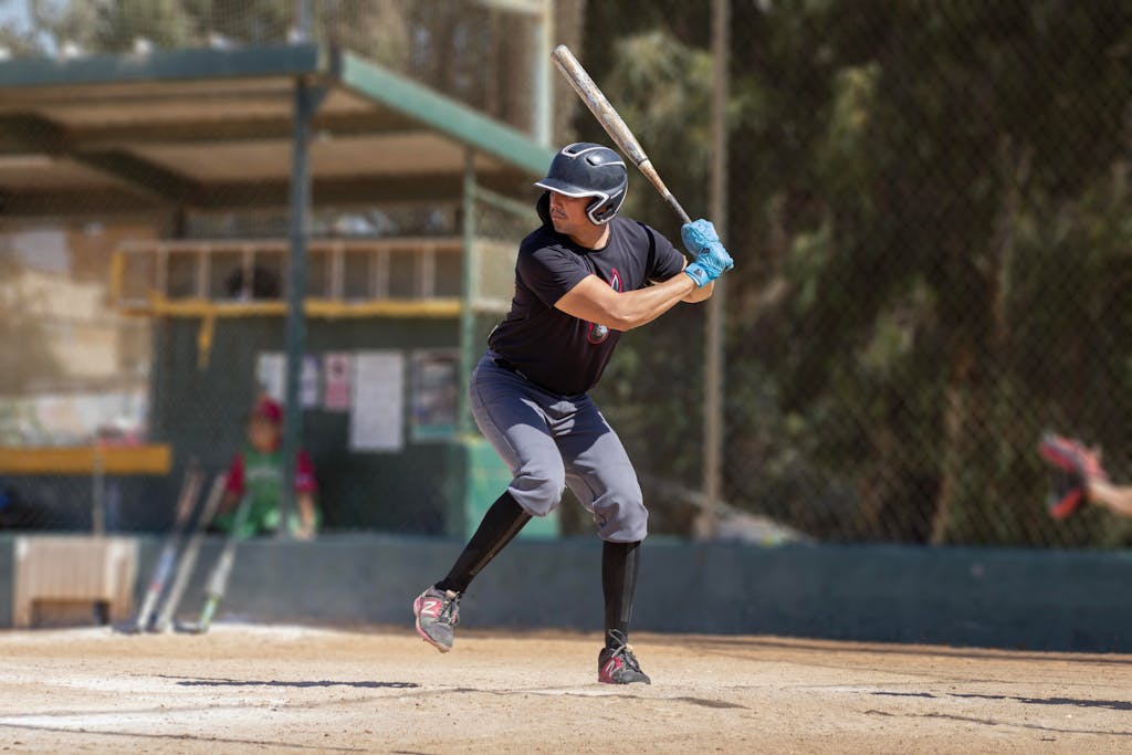 A baseball player in action at a sunlit outdoor baseball field, preparing to swing.